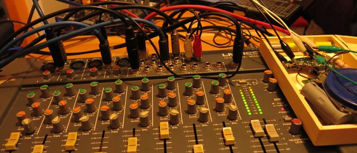 mesa de sonido de ocho canales con cables conectados entre sus entradas y salidas, encima de la mesa hay un pequeño sintetizador